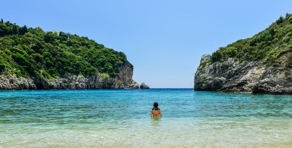 Swimmer at Agios Spyridon surrounded by green cliffs and turquoise water