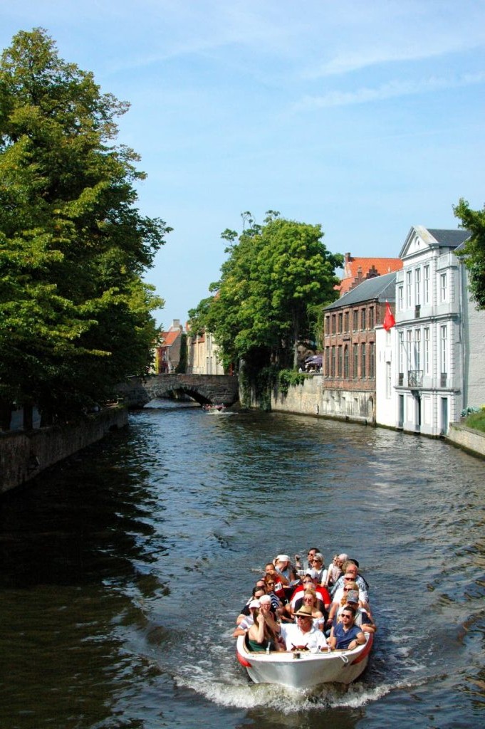 Open boat cruising a tree-lined Bruges canal