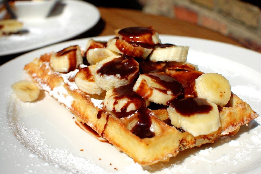 Belgian waffle topped with banana slices and chocolate sauce