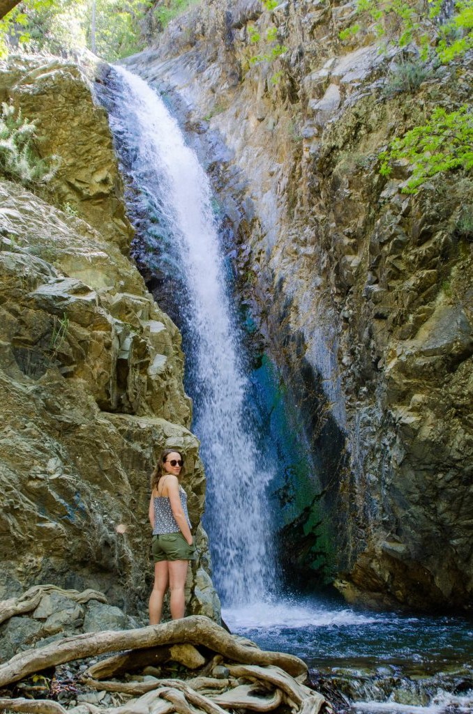 Hiker standing at the base of a tall waterfall in a narrow gorge in Cyprus.